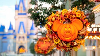 The top of a streetlamp adorned with a fall themed wreath surrounding a pumpkin Mickey Mouse face and ears