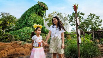 Two Guests walk hand in hand past the tall Te Fiti topiary at the Journey of Water, Inspired by Moana attraction