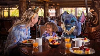 Stitch greeting a child and an adult while they enjoy breakfast at Ohana in Disney's Polynesian Village Resort