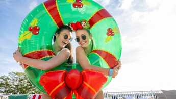 Two women peeking through and embracing an inner tube decorated to look like a Christmas wreath