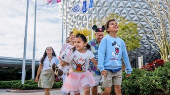 Una familia de 6 integrantes camina de a dos, tomados de las manos, cerca de Spaceship Earth en EPCOT