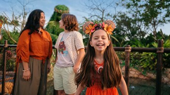 A child smiling while wearing a Minnie Mouse ear headband as 2 Guests stand nearby