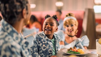A little girl smiles while Cinderella smiles next to her