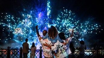 A mom and dad holding their daughter on their shoulders during a fireworks show
