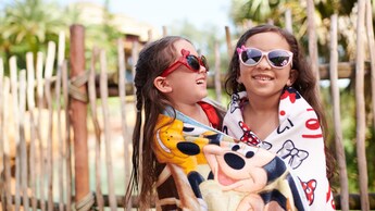 2 girls wrapped in beach towels wearing sunglasses while hugging each other