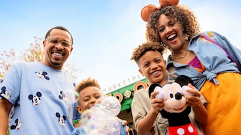 A family of 4 wearing Disney themed apparel holding a bubble wand and a Mickey Mouse plush toy