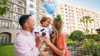 Two adults smiling as they hold a child with a Mickey Mouse balloon