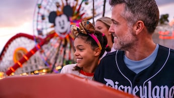A father and daughter smiling together with Pixar Pal A Round in the distance