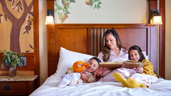A mother reading to her 2 children in bed at Disney’s Grand Californian Hotel & Spa