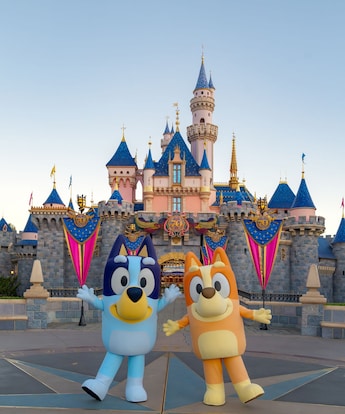 Bluey and Bingo pose together in front of Sleeping Beauty Castle