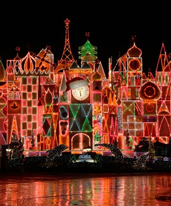 The façade of it’s a small world holiday at night with signs reading ‘it’s a small world and happy holidays’ and an illustration of children