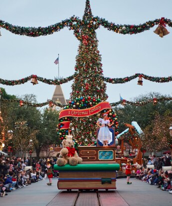 A ballerina and a giant teddy bear in front of a Christmas tree with a banner reading A Christmas Fantasy on a holiday themed parade float