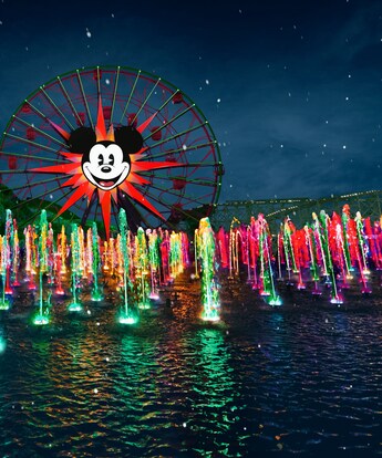 The World of Color, Season of Light nighttime holiday spectacular at Disney California Adventure Park, with many synchronized fountains spouting water and the Pixar Pal A Round Ferris wheel in the background
