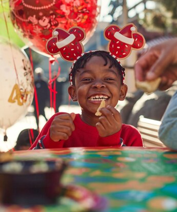 A smiling young girl in a Santa themed Minnie bow eating a snack chip