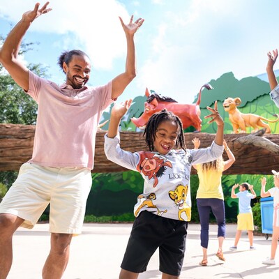Family dances in front of larger than life Pumba, Timon and Simba crossing a log