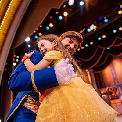 Une jeune fille déguisée en Belle serrant le Prince Adam dans ses bras