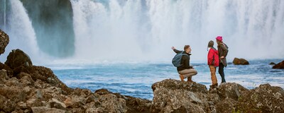 3 people on a boulder overlooking a waterfall in Iceland