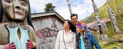 A family standing by traditional Native American totem poles and buildings