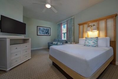 A Disney’s Vero Beach Resort hotel room with a bed, TV, dresser and ceiling fan	
