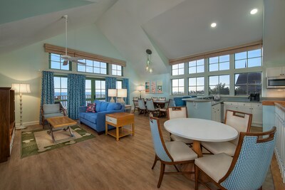 A large open room with a vaulted ceiling that includes a kitchen, 2 tables and a den