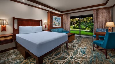 A Deluxe Standard View room with a bed, a couch, 2 chairs, a table and a sliding glass door leading to a patio and a lawn