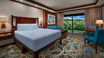 A Deluxe Standard Lake View room with a bed, a couch, 2 chairs, a table and a sliding glass door leading to a patio with a view of Seven Seas Lagoon