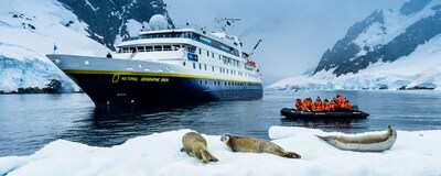 The National Geographic Sea Orion ship floating in the ocean next to a small boat filled with people watching sea lions on a piece of ice