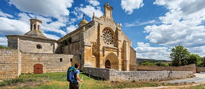 A man hiking the El Camino de Santiago, the Route of Saint James, walks by the Church of Santa Maria del Manzano in Spain