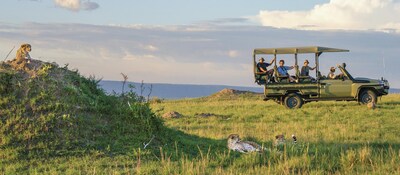 People in a covered jeep look at cheetahs resting nearby, in Tanzania