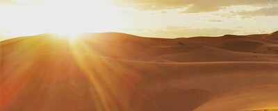 A line of people riding camels across a sand dune in the desert at sunrise