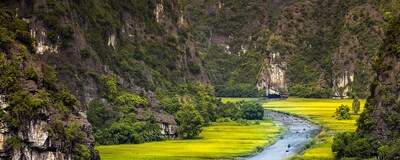 A group of sampans glide along a river winding through fields near limestone cliffs in Vietnam