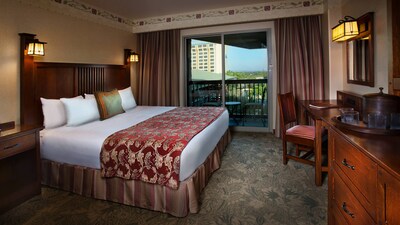 A king bed with headboard, dresser with TV, desk and chair and glass doors with a patio beyond 