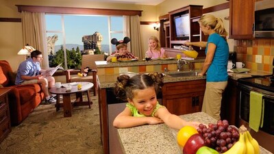 Three children eat breakfast while the mom pours a glass of juice and dad reads a newspaper