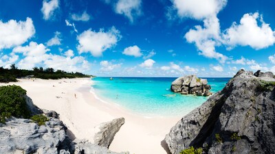 A sandy beach with large boulders, dunes and beachgoers