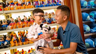 A father and his young son who is holding a Mickey Mouse plush toy, in a toy shop