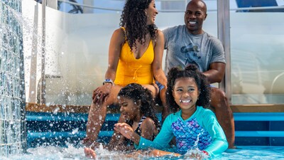 Two young girls sitting with their parents and splashing in shallow water on a Disney cruise ship