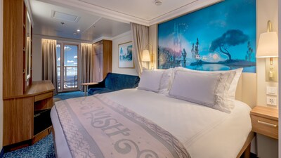 A queen bed, 2 lamps, 2 nightstands, a sofa, a mirror, shelving and a balcony