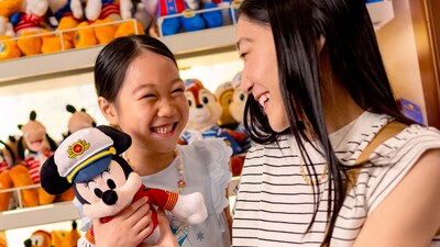A mother and her young daughter, embracing and holding a Minnie Mouse plush toy in a toy shop