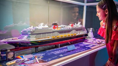 A girl looks at a model replica of the Disney Wish cruise ship