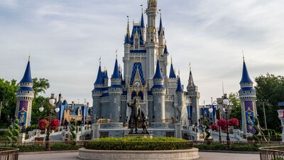 A statue of Walt Disney and Mickey Mouse in front of Cinderella Castle