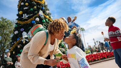 A mother bending down to kiss her daughter in front of a Christmas tree