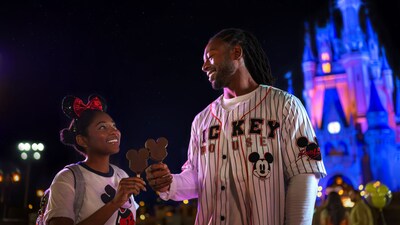Two smiling young adults wearing Mickey Mouse apparel and holding Mickey Mouse ice cream bars in front of Cinderella Castle