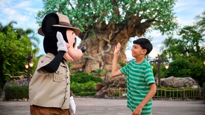 A young boy high fiving Mickey Mouse in front of the Tree of Life at Disney's Animal Kingdom theme park
