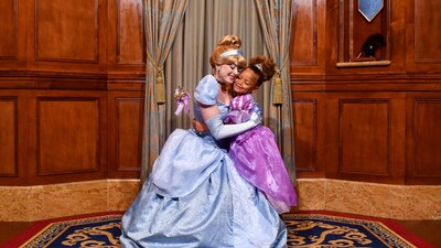 A young girl dressed like a princess hugs Cinderella