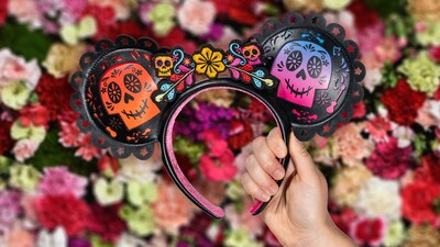A hand holding a Coco inspired Minnie Mouse ear headband in front of a wall of flowers