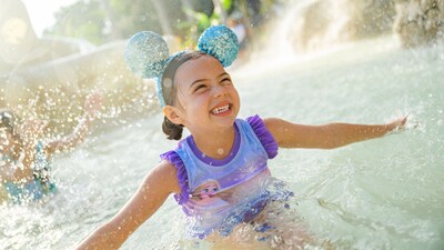 A smiling young girl in a Minnie Mouse ear headband splashes her hands in the water as she enjoys the Typhoon Lagoon Surf Pool 