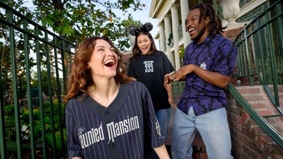 Guests smile in front of The Haunted Mansion, wearing a baseball jersey, button down shirt and T-shirt themed to the attraction