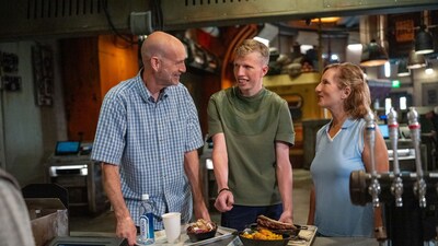 A man and woman smile at a teenage boy while picking up food in Star Wars: Galaxy’s Edge.