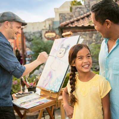 Una niña pequeña sonríe a su familia mientras observa al artista David Buckley pintar una imagen de Mickey Mouse