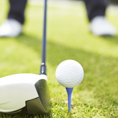 2 feet standing over a golf club positioned to hit a golf ball on a tee